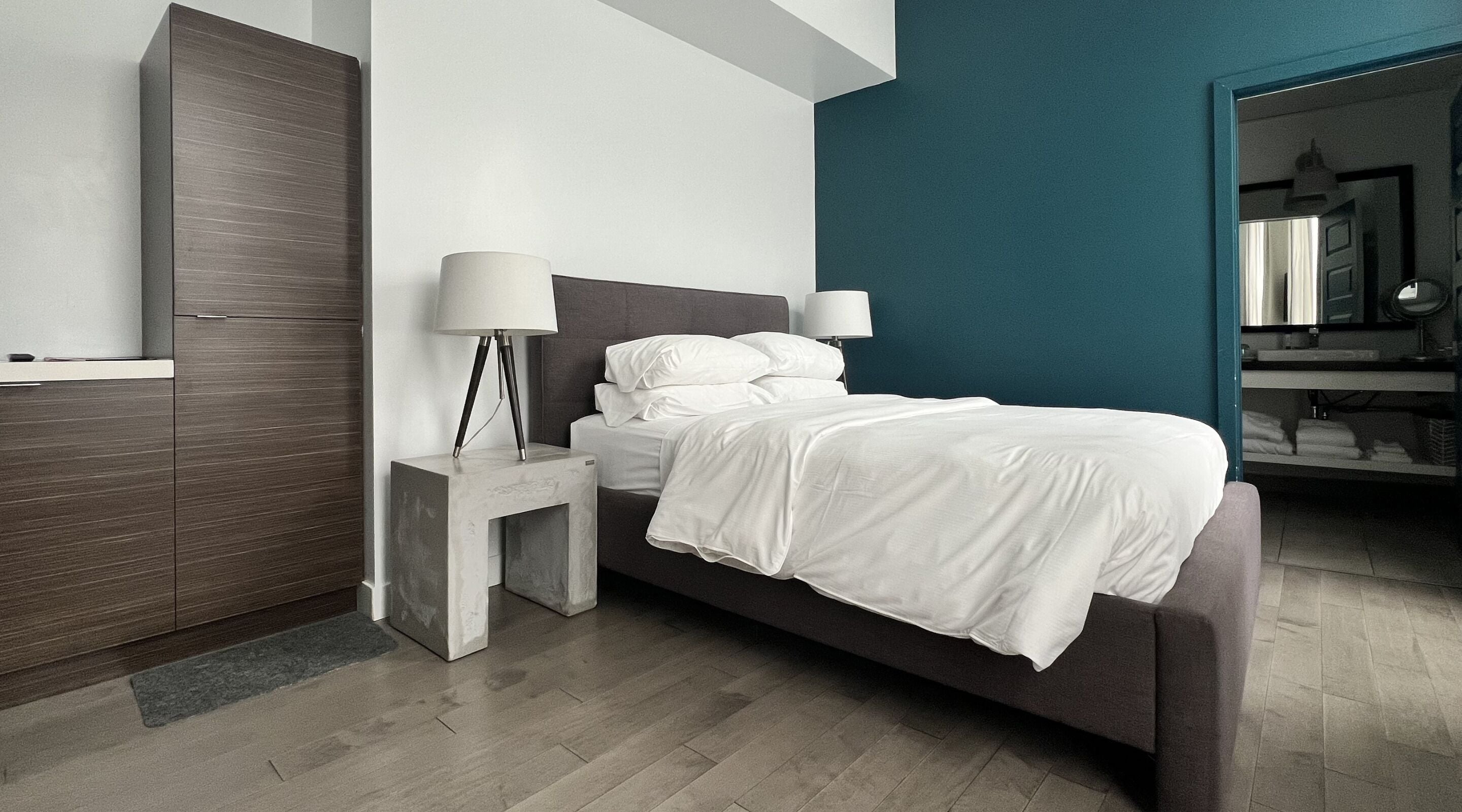 A modern bedroom with a bed, nightstands, a wardrobe, and a bathroom visible in the background.
