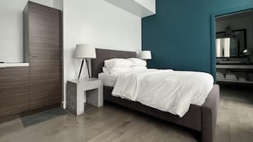 A modern bedroom with a bed, nightstands, a wardrobe, and a bathroom visible in the background.