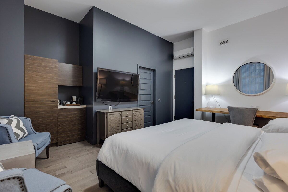 A modern hotel room with a large bed, a TV, a desk, and a chair.