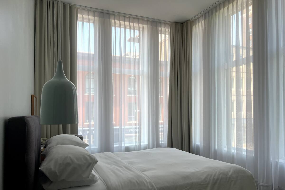 A hotel room with a bed, a lamp, and sheer curtains.