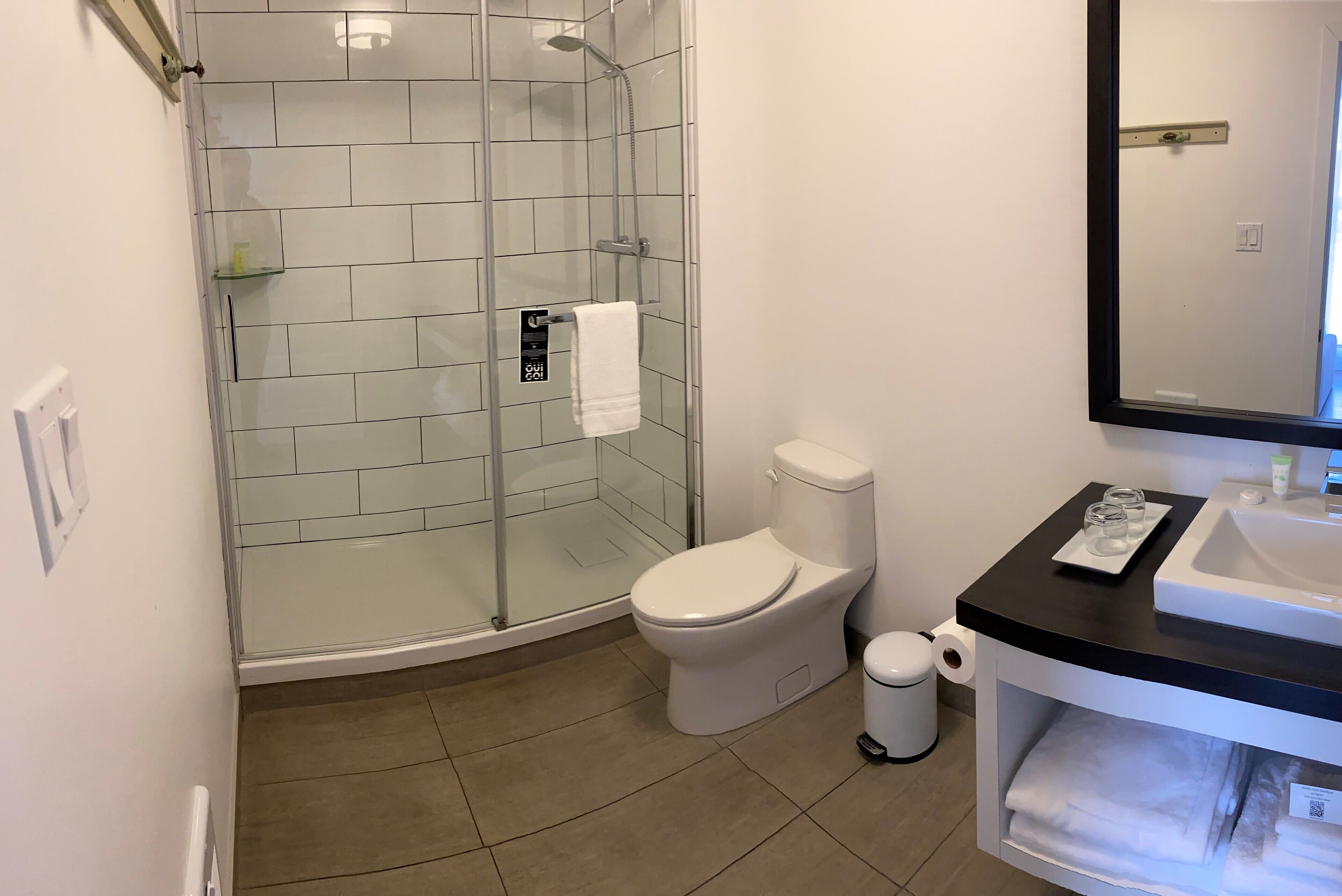 Un bagno moderno con doccia vetro, toilette, lavandino e specchio.