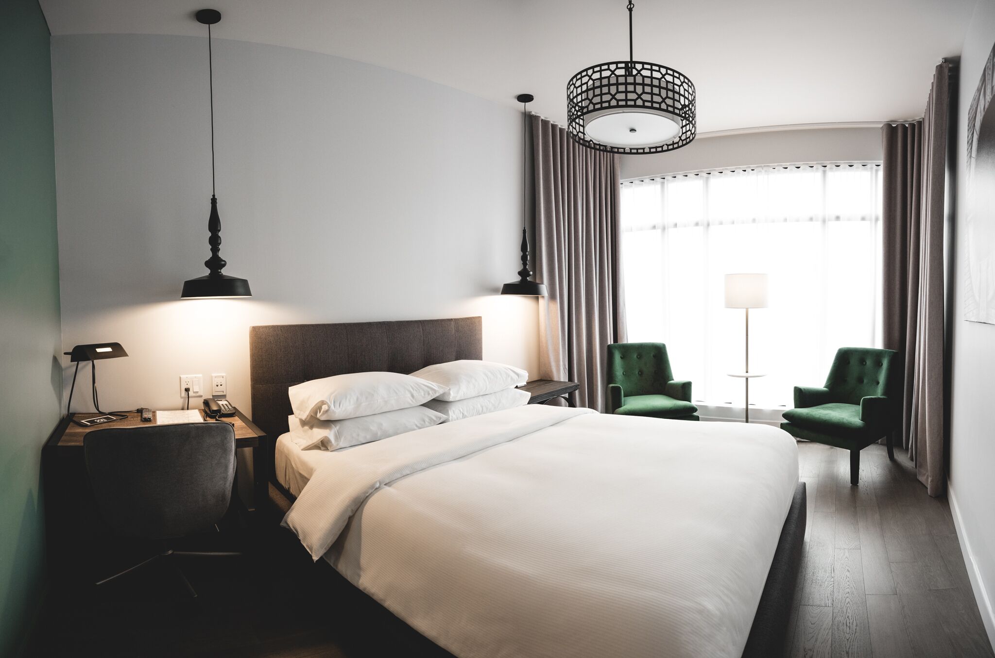 Een hotelkamer met een groot bed, een bureau met lamp, een stoel en een raam met gordijnen.