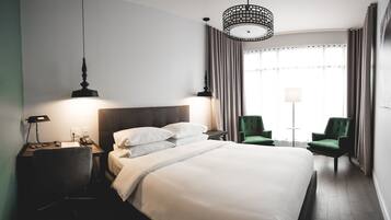 Een hotelkamer met een groot bed, een bureau met lamp, een stoel en een raam met gordijnen.