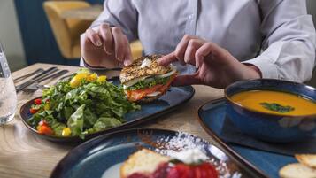 En person håller i en smörgås, och bredvid finns en sallad och en skål med soppa på bordet.