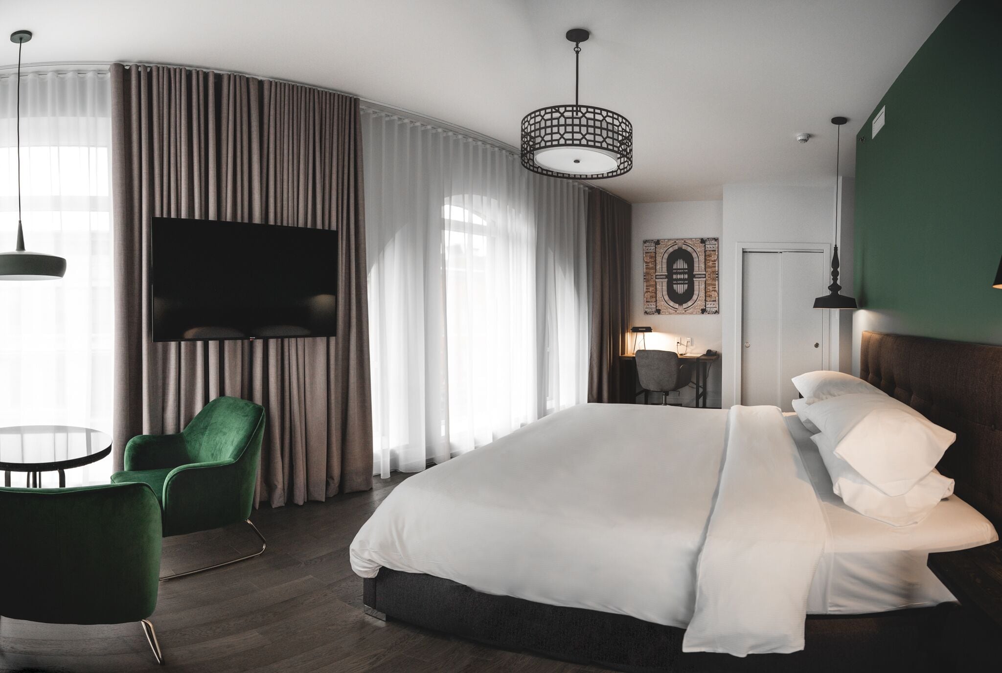 A modern hotel room with a large bed, green armchair, and a flat-screen TV.