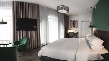 A modern hotel room with a large bed, green armchair, and a flat-screen TV.