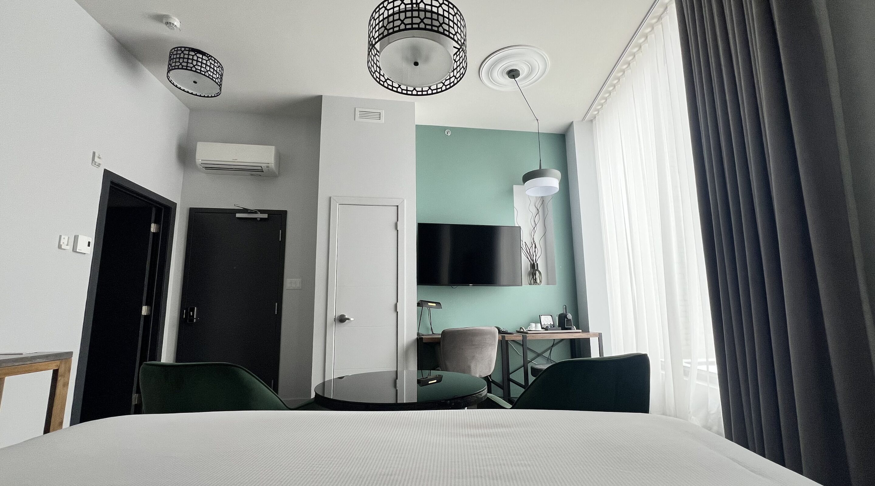 Habitación de hotel con cama, escritorio, silla, televisor y ventana con cortinas.
