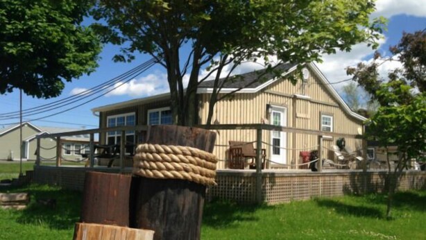 Ein hölzerner Pfosten, umwickelt mit Seil, ein Haus im Hintergrund und eine Rasenfläche.