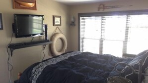 Ein Schlafzimmer mit einem Bett, einem Fernseher, einem Fenster mit Jalousien, einer Wandregal und einem runden Gegenstand an der Wand.