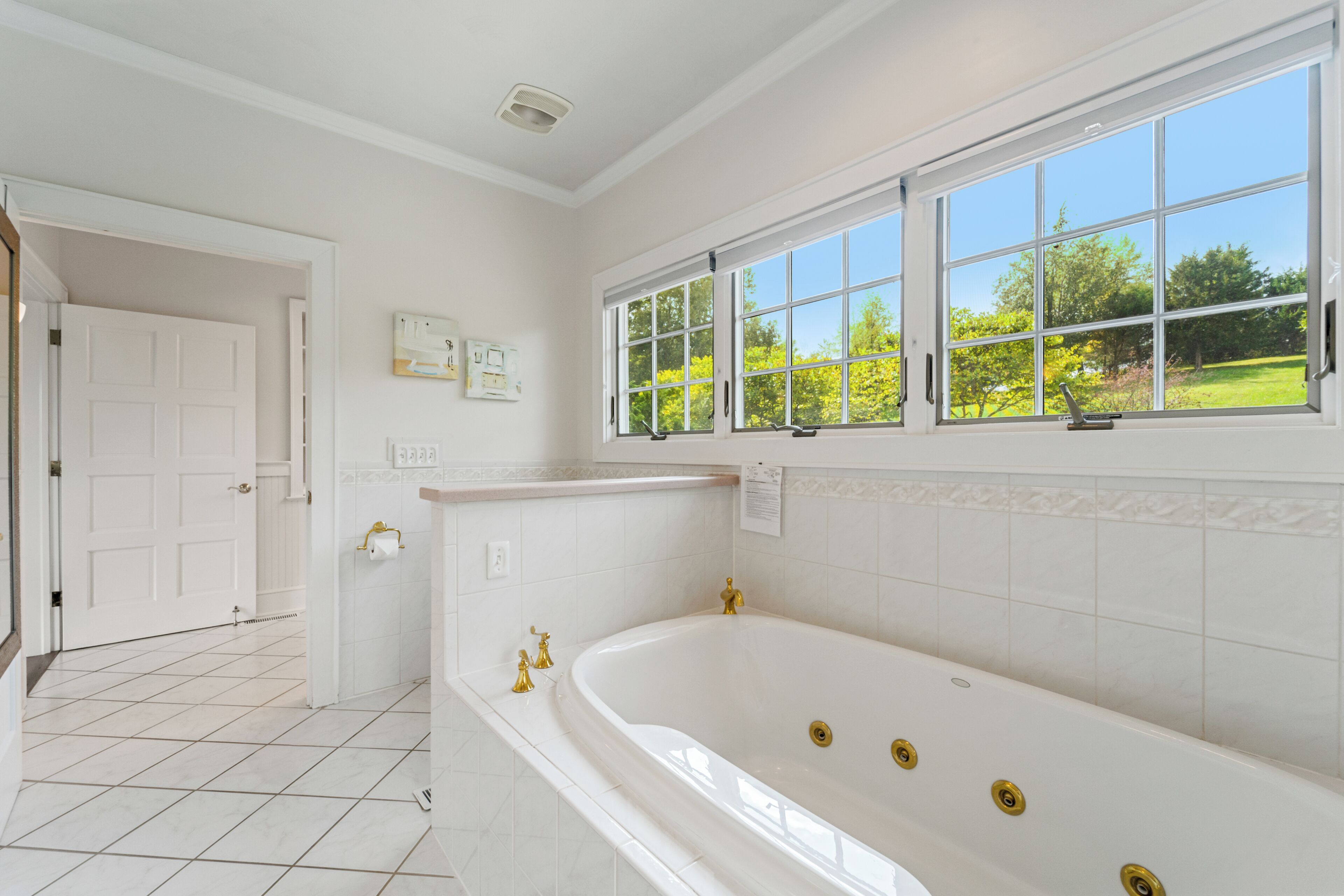 A bathroom with a large bathtub, a window with a view of greenery, and white tiled walls.