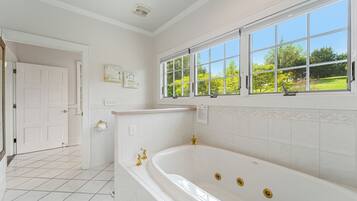 A bathroom with a large bathtub, a window with a view of greenery, and white tiled walls.