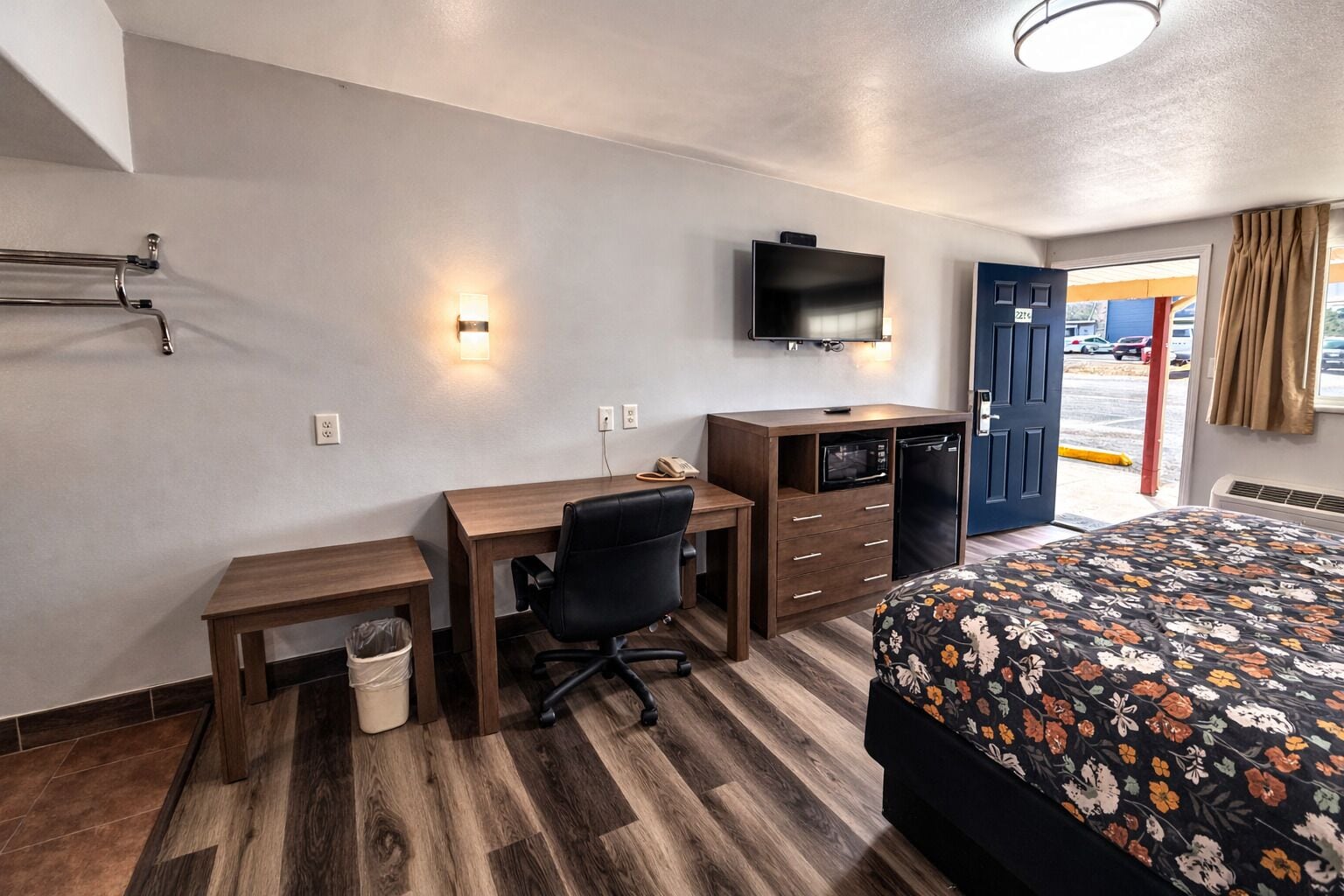 Habitación de hotel con cama, escritorio, silla, televisor y puerta que da al exterior.