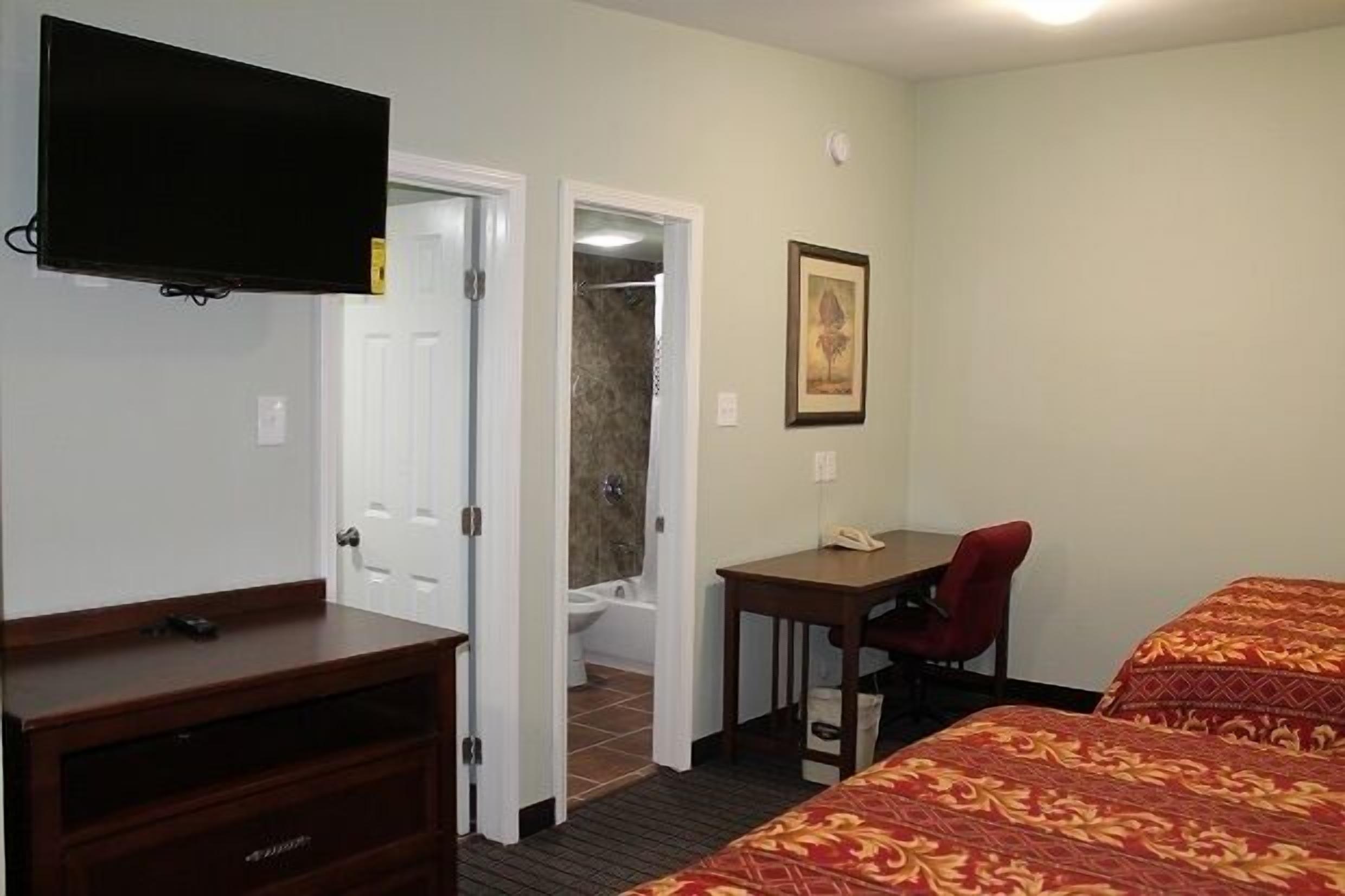 Habitación de hotel con televisión, escritorio con silla, cama y baño visible a través de una puerta abierta.