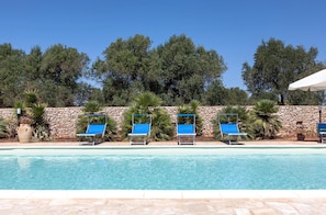 A poolside area with a stone wall, blue lounge chairs, and a clear blue pool. - Casale Tre Petre (Galatone)