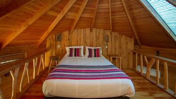 A cozy attic bedroom with a wooden sloped ceiling, a large bed with colorful bedding, and a skylight.