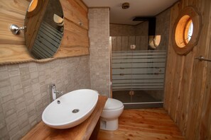 A bathroom with a wooden vanity, a white sink, a toilet, and a glass-enclosed shower. - Cabañas Agua Viva (Villarrica)