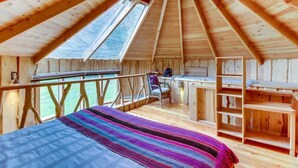 Una baita in legno con tetto spiovente, un letto con una coperta colorata, una scrivania e una sedia.