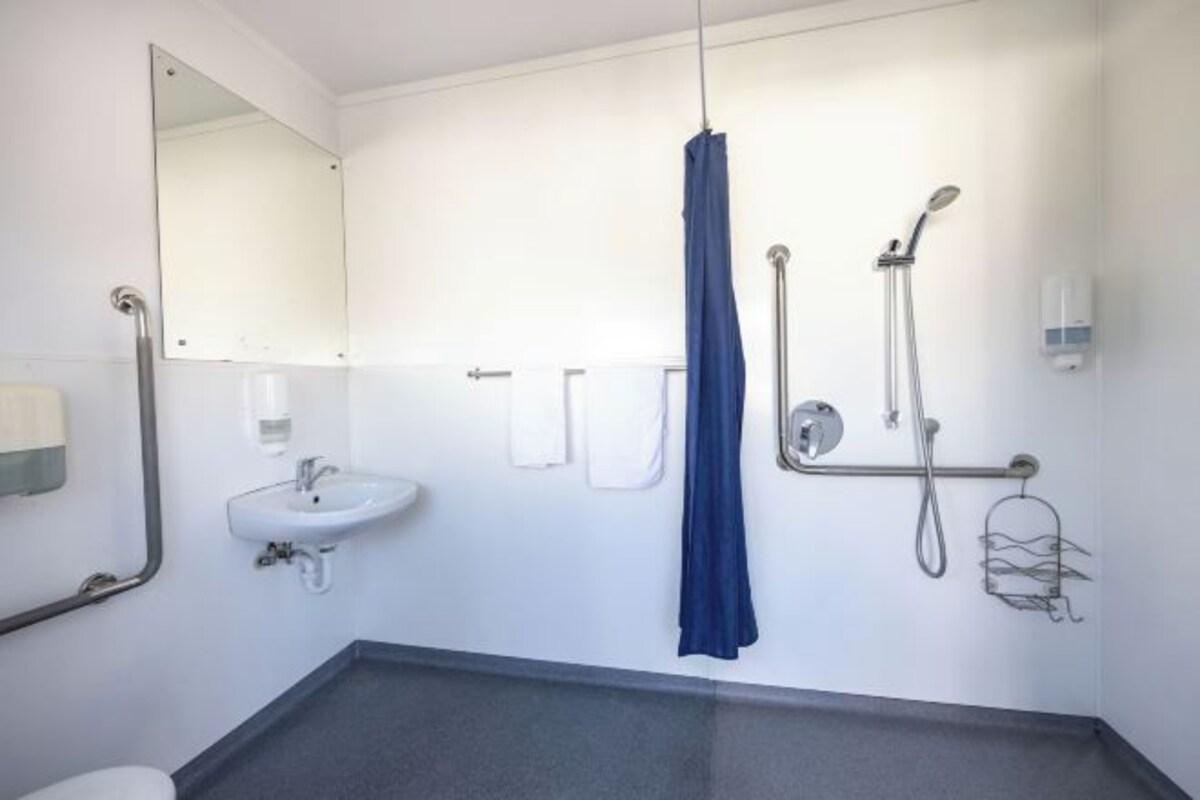 Une salle de bain moderne équipée d’un lavabo, d’un miroir, d’un porte-serviettes, d’une douche et de barres d’appui.