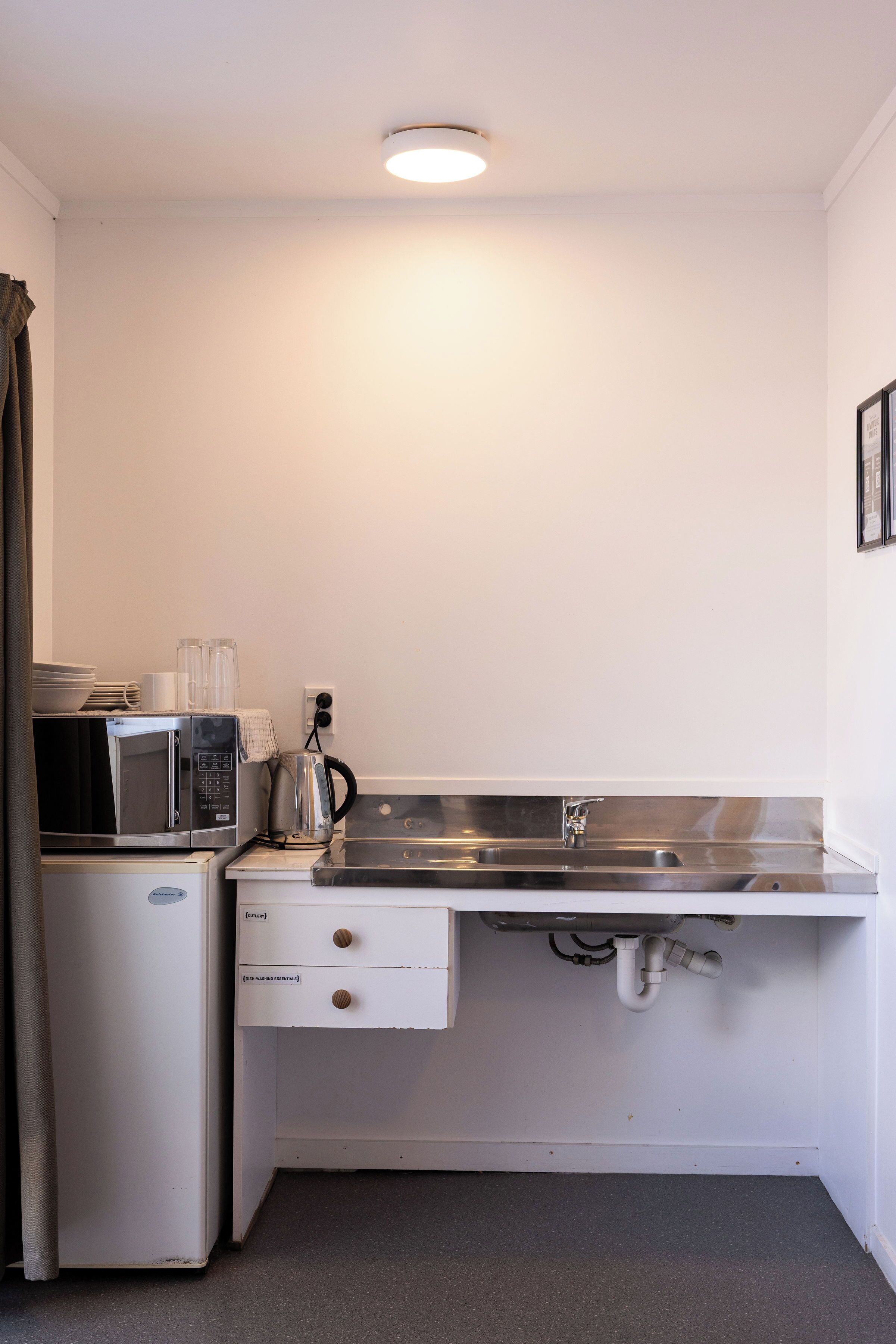 A compact kitchenette with a microwave, kettle, and sink.