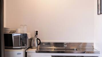 A compact kitchenette with a microwave, kettle, and sink.