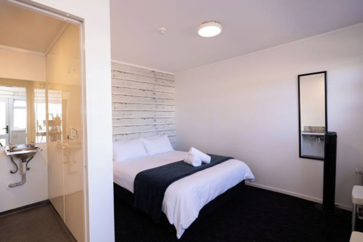 Habitación de hotel con cama, mesita de noche, espejo y baño con lavabo e inodoro.