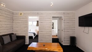 Una habitación con paneles de madera, un sofá marrón, una mesa de centro de madera, una cama, un baño y un televisor montado en la pared.