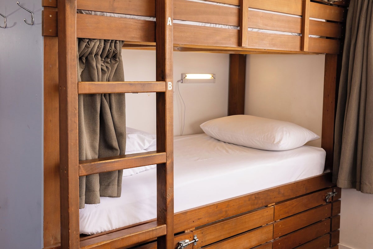 Ein Stockbett mit Holzrahmen, die untere Liege mit Matratze und Kissen sowie ein Kopfteil mit Leuchte.