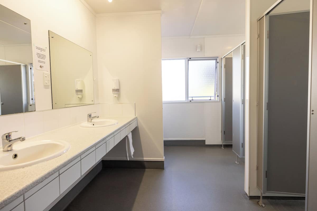 Ein helles, modernes Badezimmer mit zwei Waschbecken, einem großen Spiegel und einem Fenster für natürliches Licht.