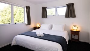 Una cama bien hecha con ropa de cama blanca y un acento azul oscuro, dos lámparas de noche y un ventanal con cortinas.