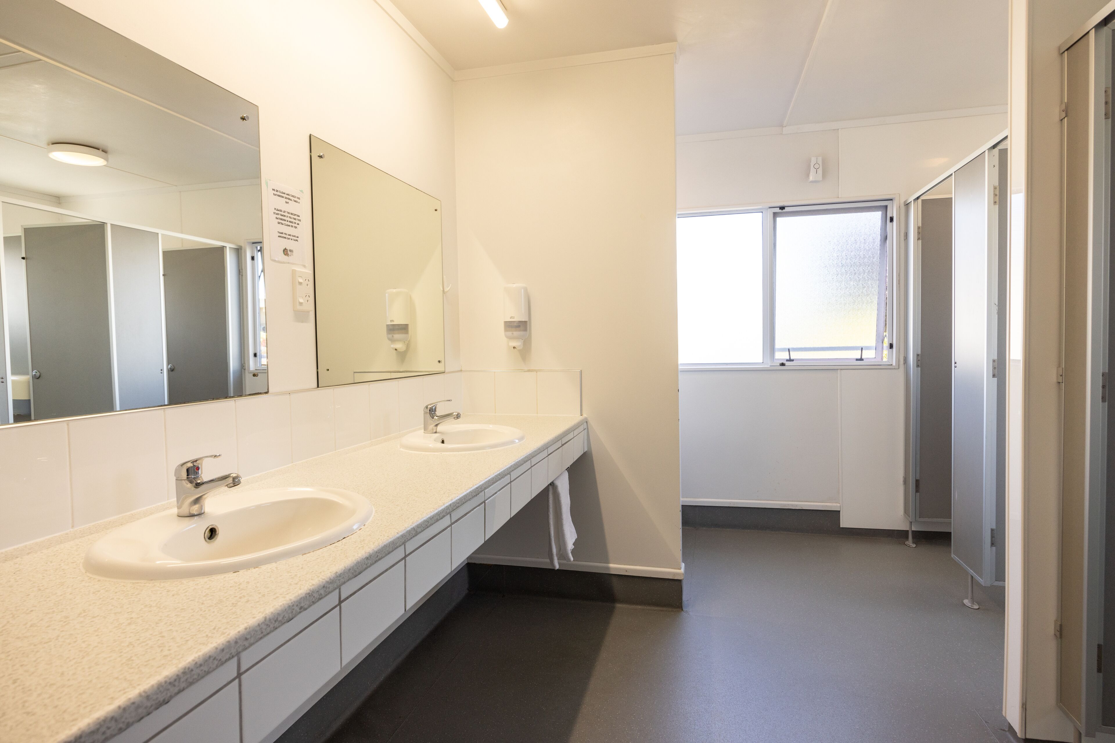 A clean, modern bathroom with two sinks, a large mirror, and a window providing natural light.
