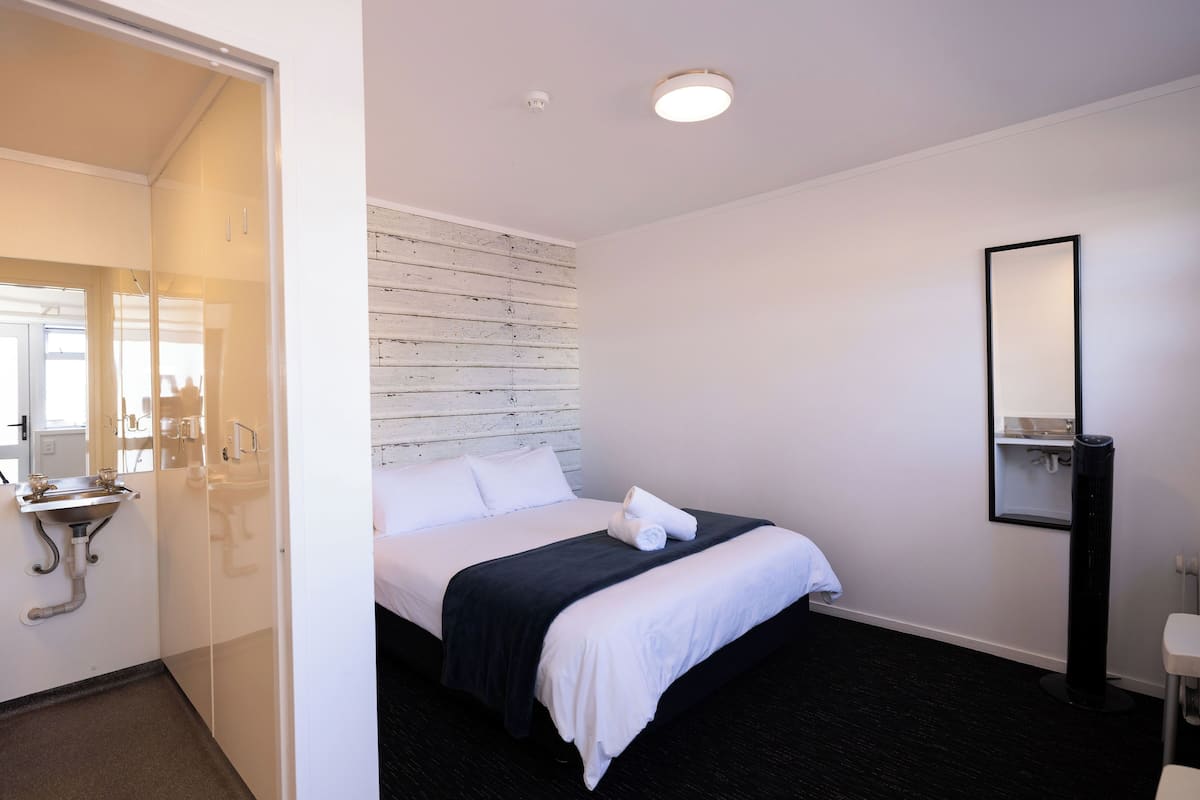 Ein Hotelzimmer mit Bett, Nachttisch, Spiegel, Waschbecken und Fenster.