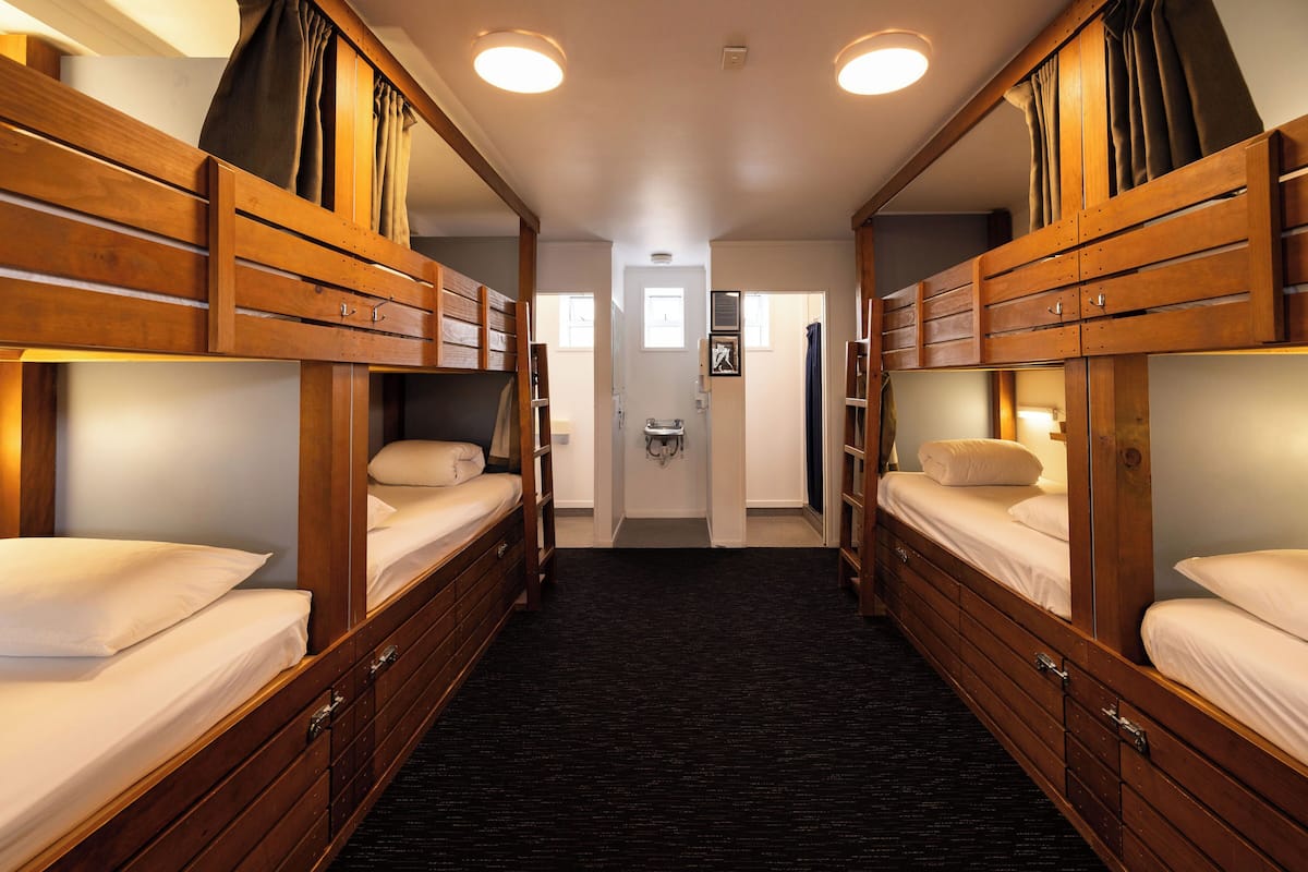 Ein Hotelzimmer mit Etagenbetten, einem schwarzen Teppich und einer Tür zu einem Flur.