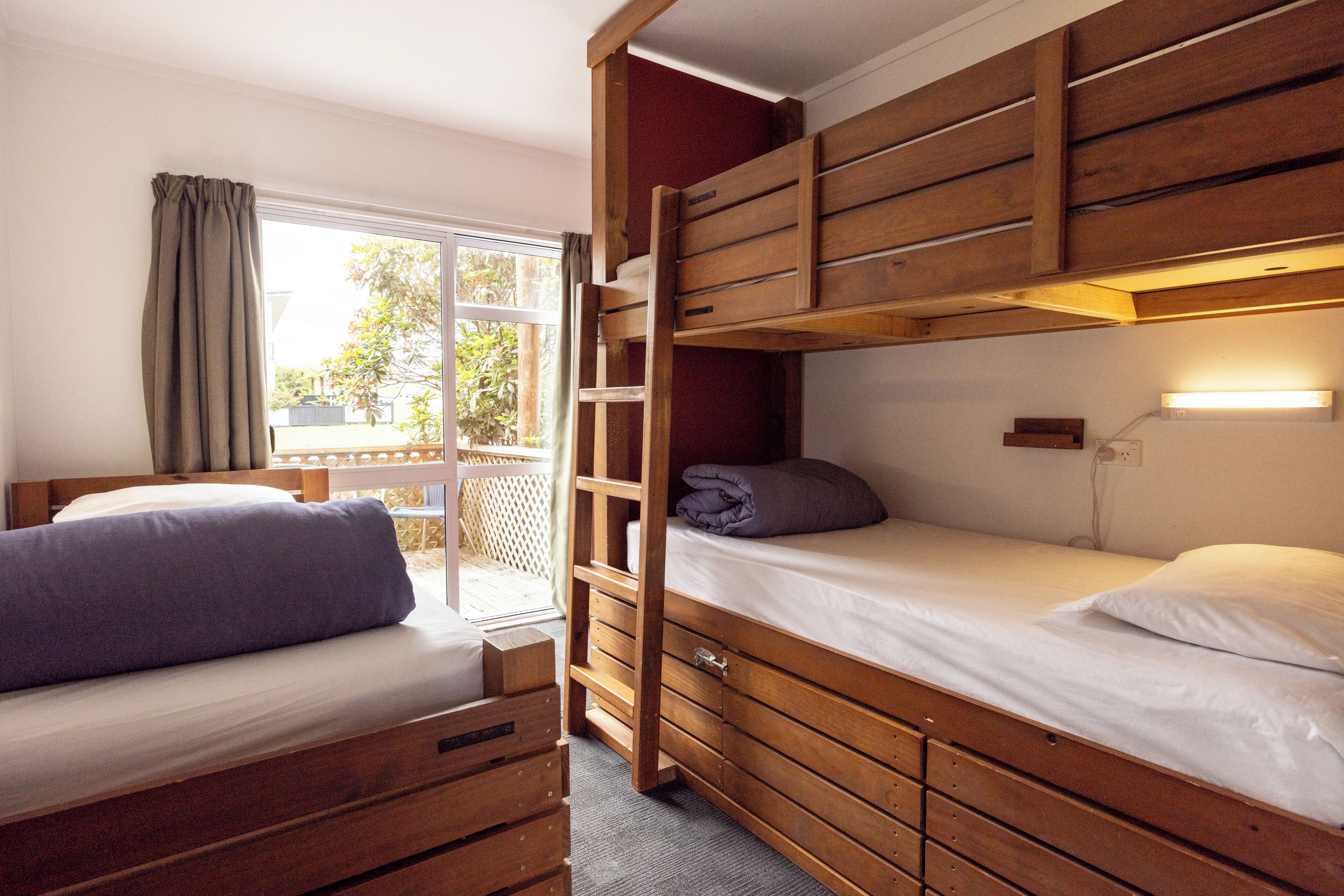 Een kamer met twee houten stapelbedden, een raam met gordijnen, en een kleine tafel met stoelen buiten.