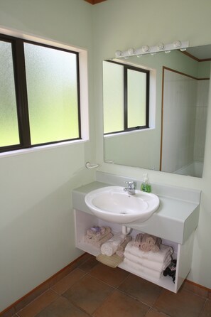 A bathroom with a white sink, a mirror above it, and a window with frosted glass. - Capeview Cottage (Tirohanga)