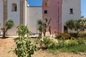 A building with a courtyard, featuring a mix of brick and plaster walls, a small staircase, and several trees.