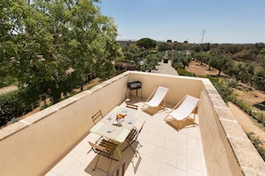 An outdoor patio with a table set for dining, surrounded by chairs and a sun lounger.