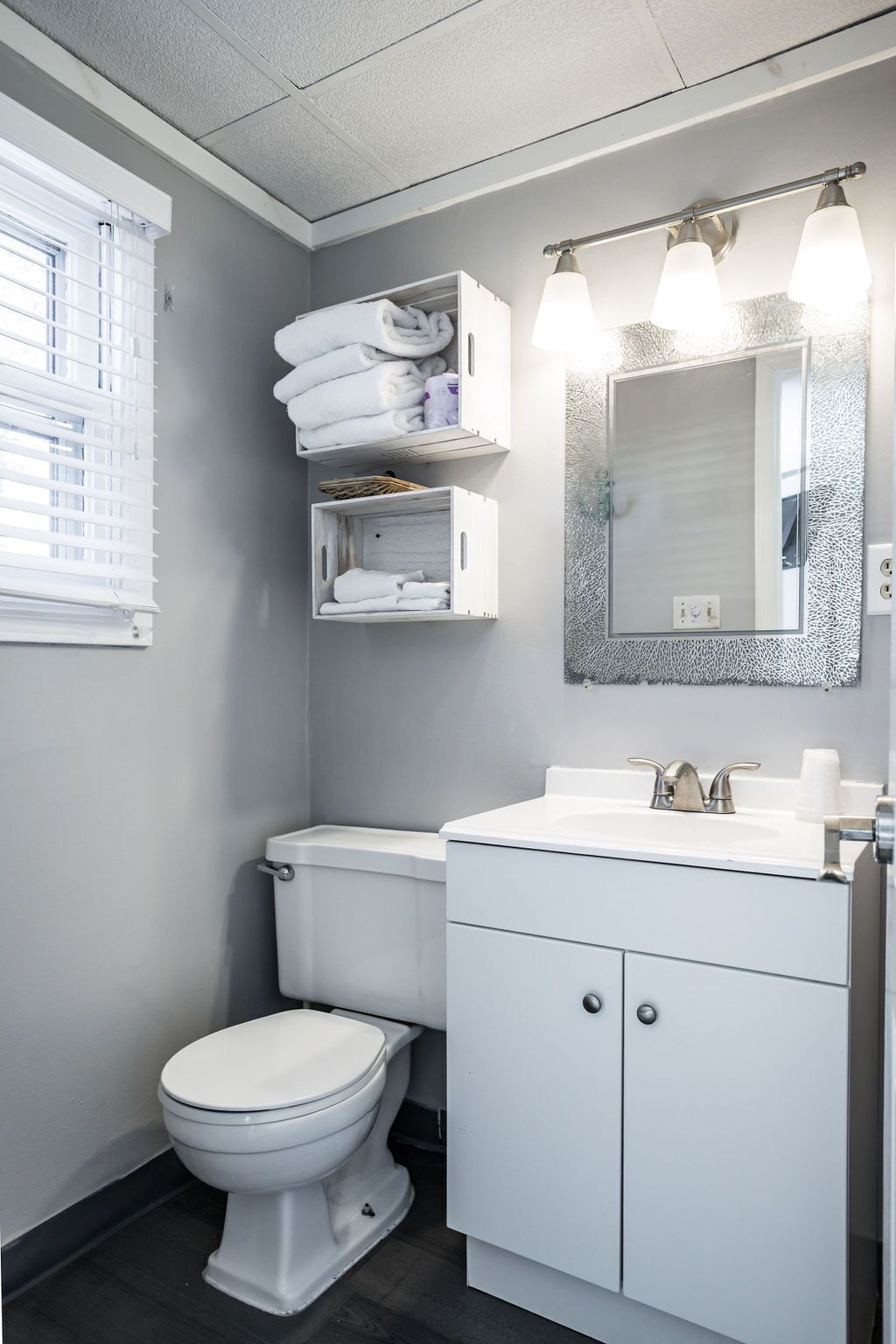 Un baño moderno con inodoro, lavamanos y tocador. Hay toallas y artículos de aseo guardados en estantes sobre el inodoro.