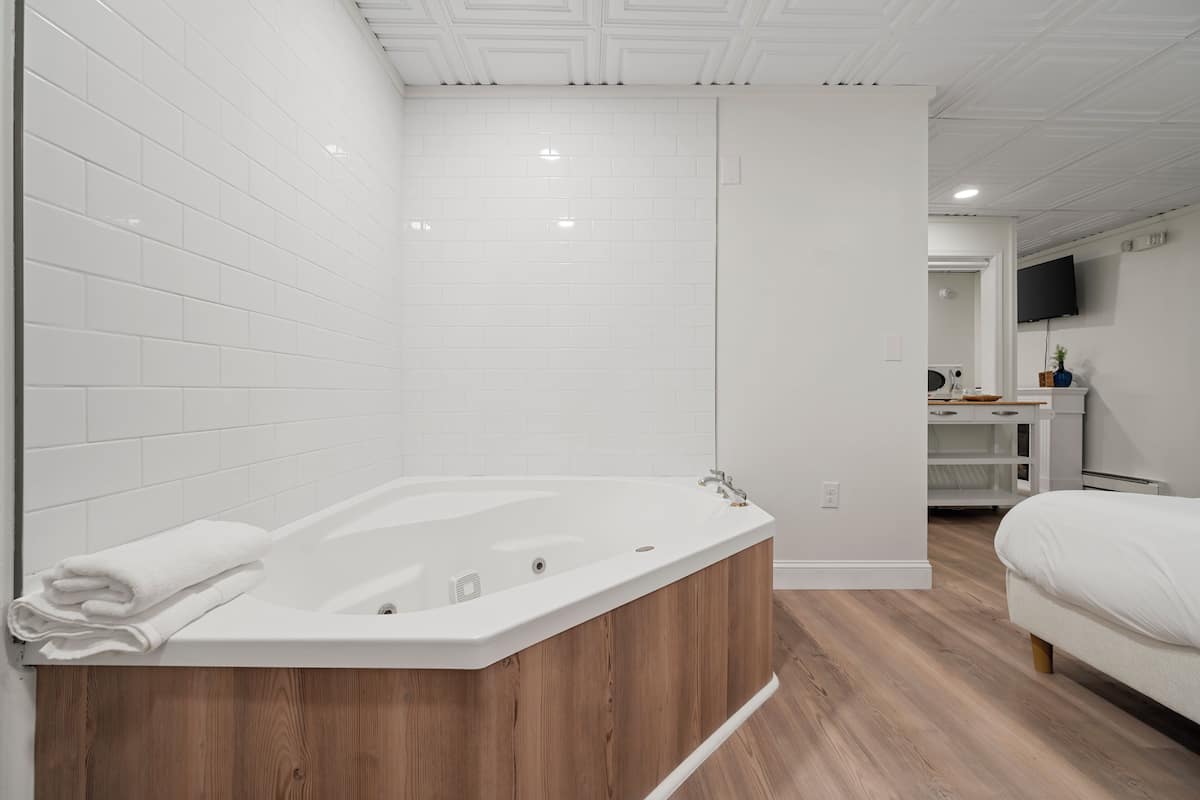 Une salle de bain moderne avec une baignoire sur pieds, un plancher en bois et des murs recouverts de carreaux blancs.