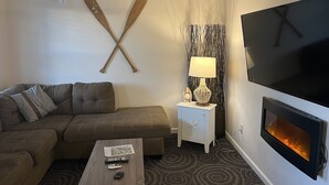 Una sala moderna con sofá, mesa de centro, televisor, chimenea y ventilador de techo.
