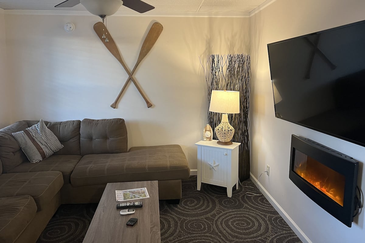 Un salon moderne comprenant un canapé, une table basse, un téléviseur, une cheminée et un ventilateur de plafond.