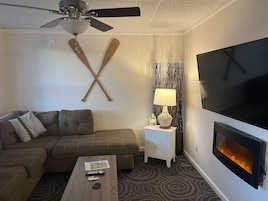 Una sala moderna con sofá, mesa de centro, televisor, chimenea y ventilador de techo.