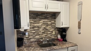 Una cocina con armarios blancos, encimera de granito, pileta de acero inoxidable y un salpicadero decorativo.
