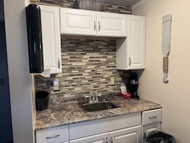 Una cocina con armarios blancos, encimera de granito, pileta de acero inoxidable y un salpicadero decorativo.