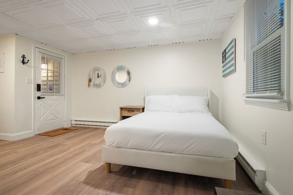 Une chambre à coucher avec un lit, une table de chevet, une porte et une fenêtre avec des stores.
