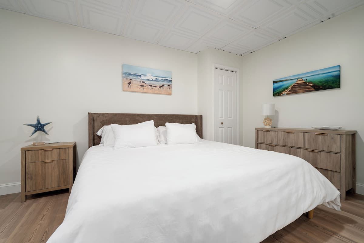 Une chambre à coucher avec un grand lit, des tables de chevet en bois, une commode et deux tableaux accrochés au mur.