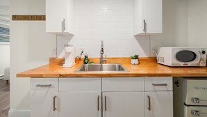 Una cocina moderna con armarios blancos, encimera de madera, pileta de acero inoxidable, microondas y una pequeña planta en maceta.