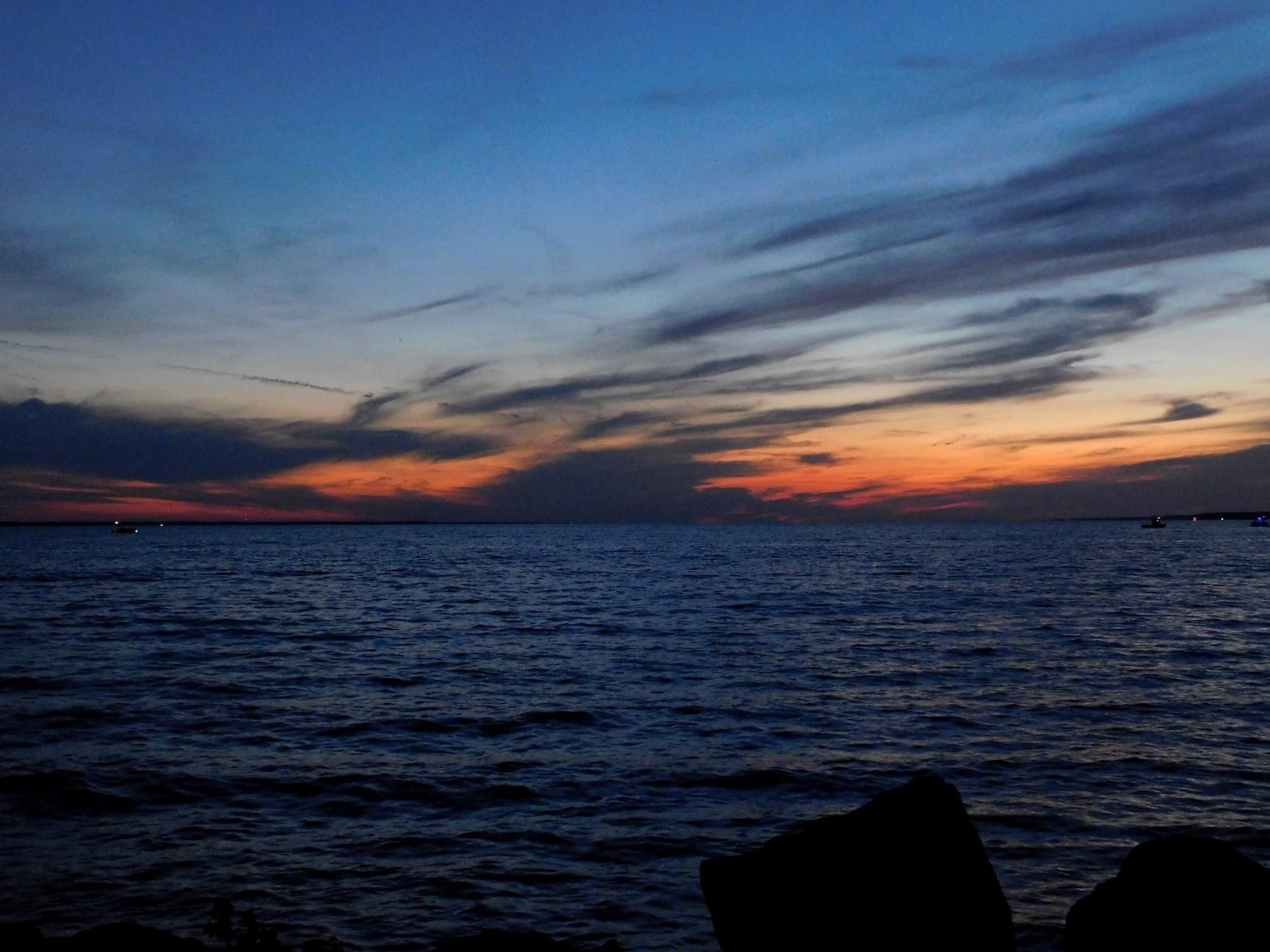A coastal sunset with calm waters and a rocky foreground.