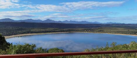 A lake with mountains in the background, a wooden deck, and dense greenery.