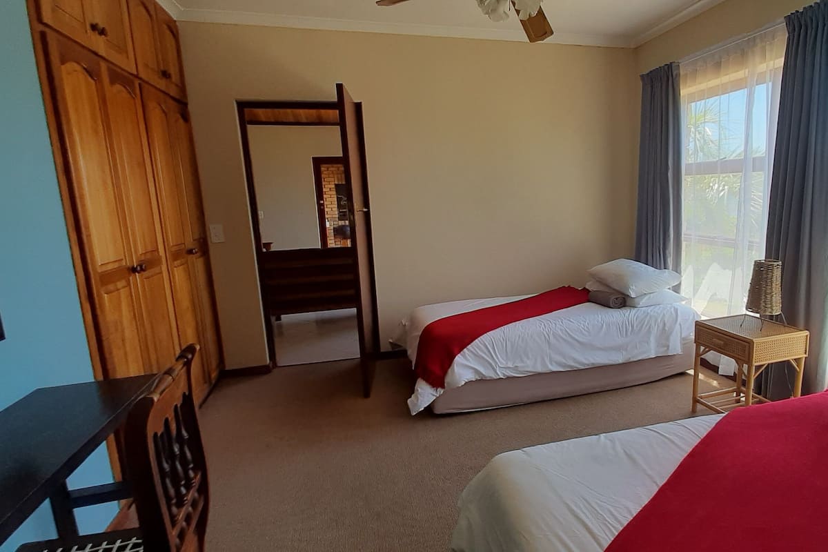 Habitación de hotel con dos camas, un armario de madera, un espejo y una ventana con cortinas.