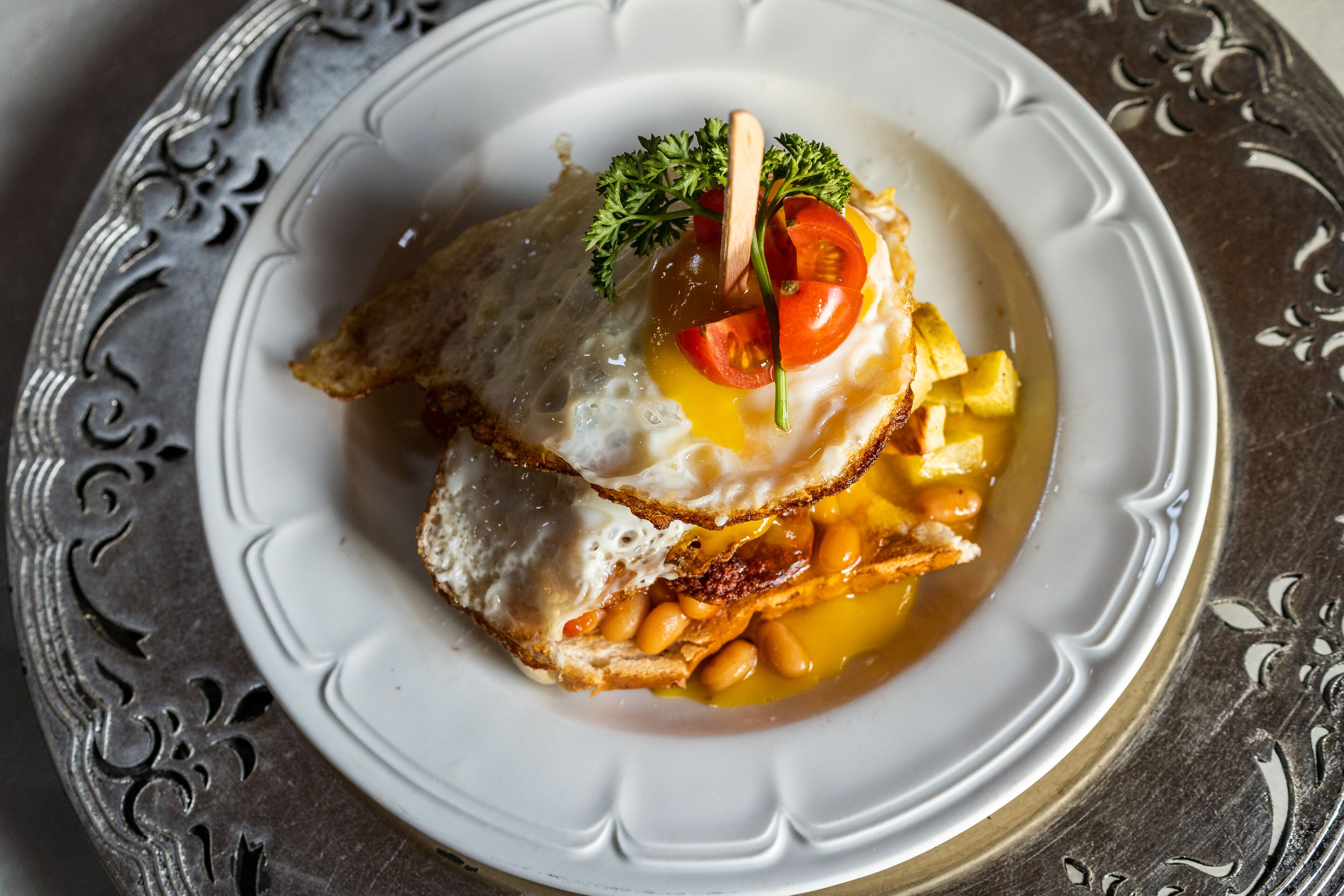A plate with a sandwich, egg, beans, and a garnish.